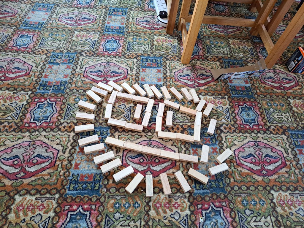 An image of a face with large eyes and a straight mouth, made of Jenga blocks, encircled by other Jenga blocks